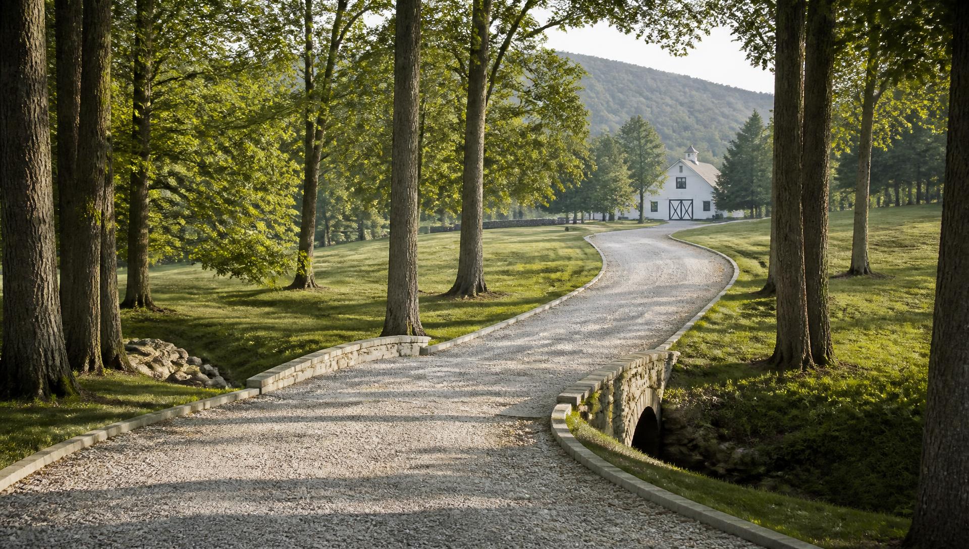 Estate Driveways & Property Access in North Georgia in North Georgia — Gravel estate driveway curving through hardwoods toward a white barn